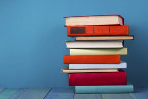 Stack of colorful books, grungy blue background, free copy space Vintage old hardback books on wooden shelf on the deck table, no labels, blank spine. Back to school. Education background